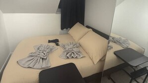 Habitació d'hotel moderna amb llit, taula petita, banqueta i mirall.