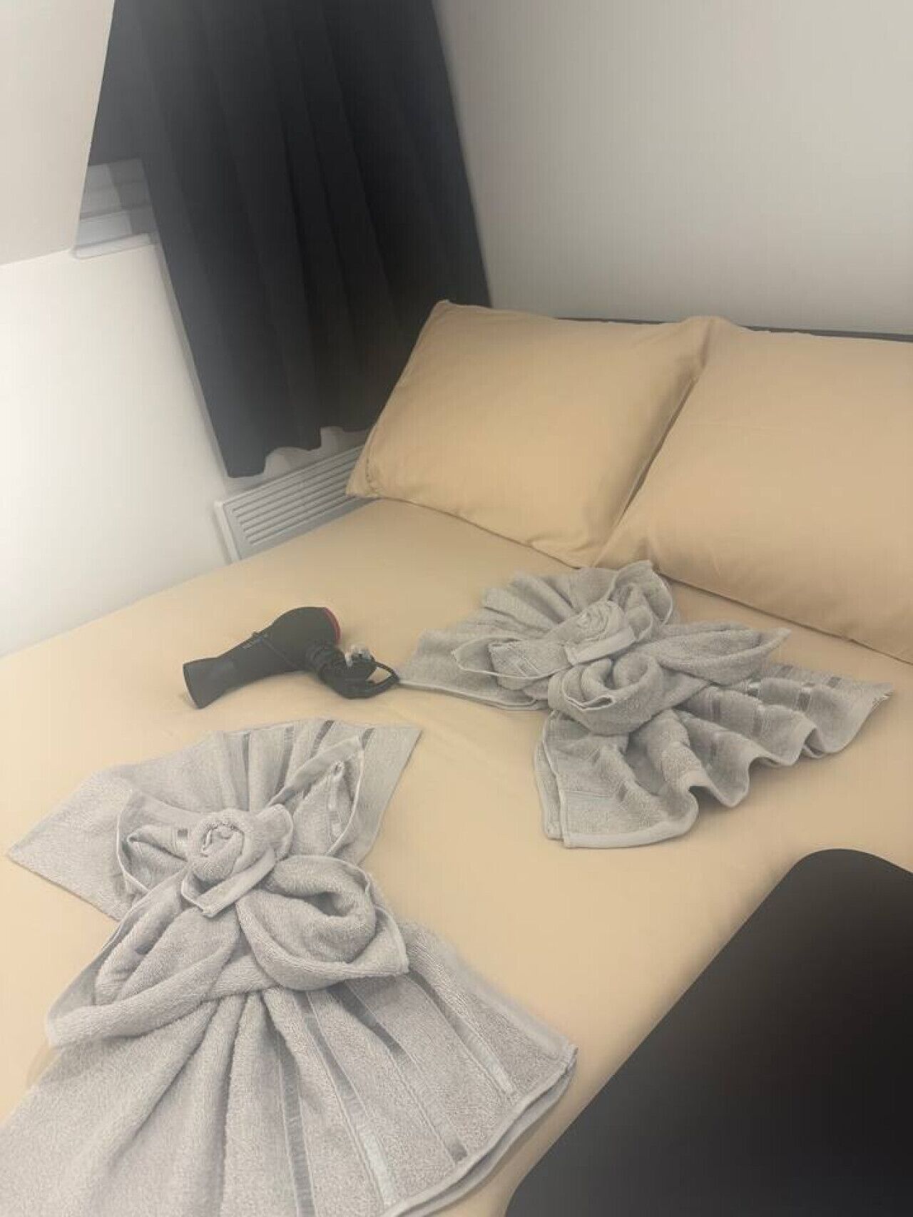 Een bed met beige beddengoed, twee kussens en twee handdoeken netjes opgemaakt.