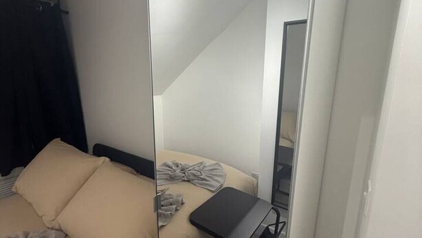 Un dormitori modern amb un llit, una taula petita i un mirall.