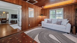 A modern living room with wooden paneling, a white sofa, and a patterned rug. - Fairmount Manor off of Lake Hollingsworth. Games, Gym, and Gather! Sleeps 8 (Lakeland)