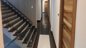 A modern interior with a glass staircase, a wooden door, and a hallway leading to a room.
