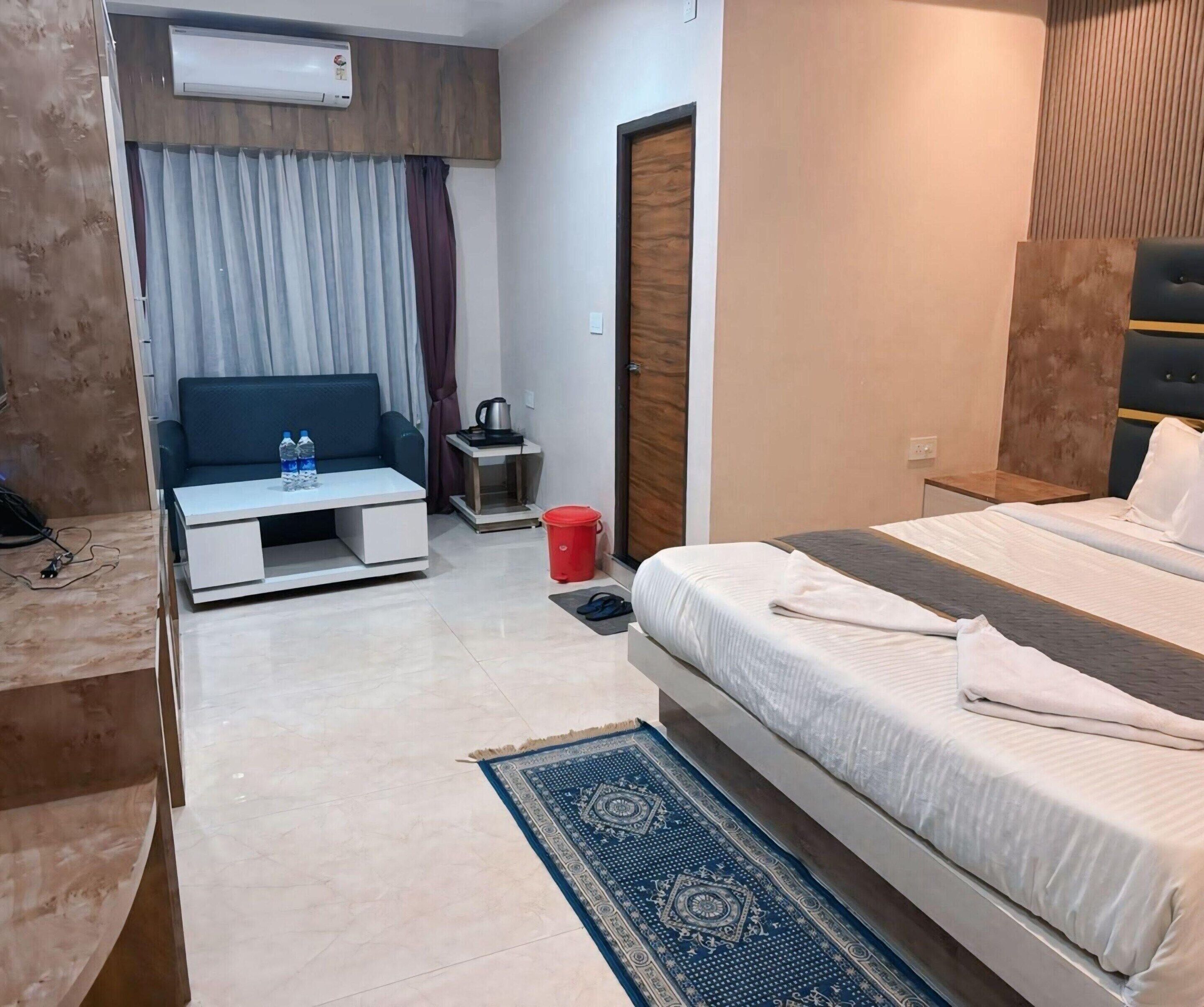 A hotel room with a bed, a sofa, a small table, a red bucket, a coffee maker, and an air conditioning unit.