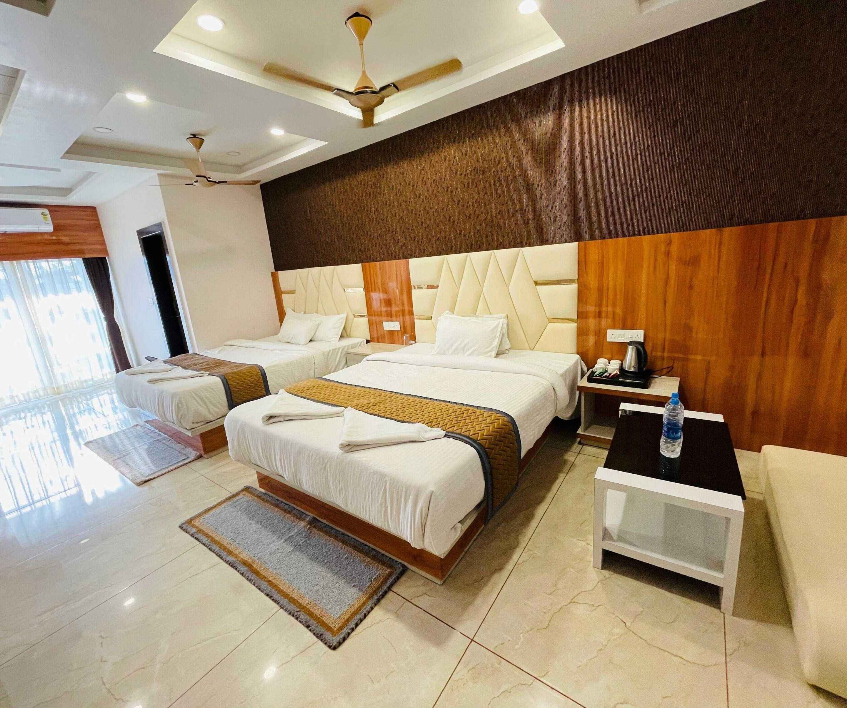 A hotel room with two beds, a ceiling fan, a small table with a water bottle, and a view of the outside.