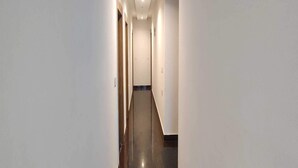 A narrow, well-lit hallway with white walls and a polished floor.
