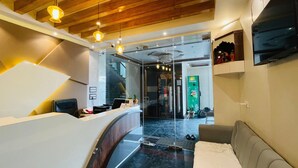 A modern hotel lobby with a reception desk, a sofa, a staircase, and a refrigerator.