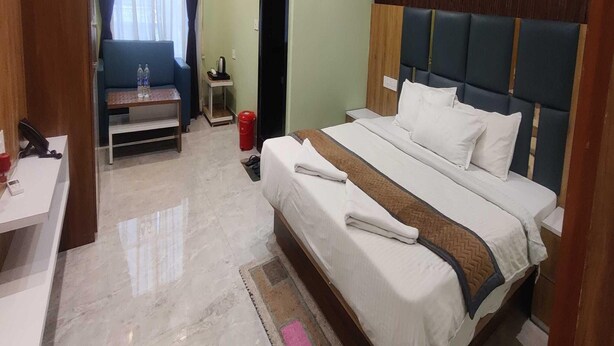 A hotel room with a bed, a desk, a chair, a small table, and a window with curtains.