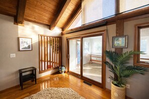 Quarto com piso de madeira, porta de correr de vidro, uma mesinha, planta em vaso e um quadro na parede.