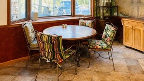 Een eetgedeelte met een ronde tafel, gestreepte stoelen, een stenen muur, een raam met uitzicht en een muurschildering van palmbomen.