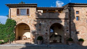 A stone building with arched doorways, potted plants, and a gravel driveway. - Villa le Murate by MMega (Montaione)