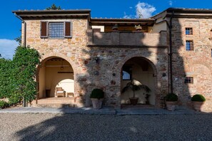 A stone building with arched doorways, potted plants, and a gravel driveway. - Villa le Murate by MMega (Montaione)