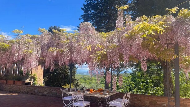 An outdoor dining area with a table and chairs, surrounded by flowering trees and a scenic view. - Villa le Murate by MMega (Montaione)