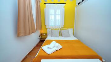 Una habitación de hotel con cama, mesita de noche, lámpara y aire acondicionado.