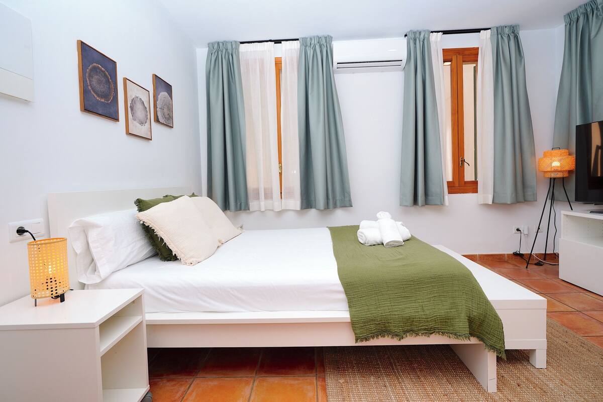 A bedroom with a bed, white nightstands, a lamp, a television, and artwork on the wall.