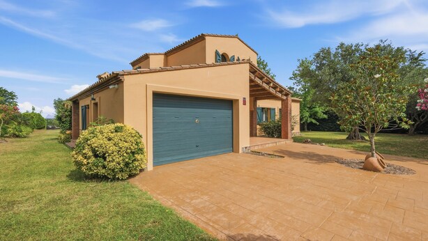 Ein eingeschossiges Haus mit Garage, umgeben von einem gepflegten Rasen und einigen Bäumen.