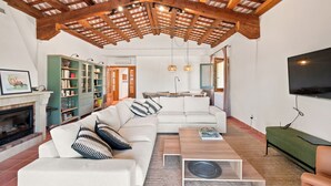 Ein Wohnzimmer mit Holzbalkendecke, einem weißen Sofa, einem Couchtisch und einem an der Wand befestigten Fernseher.