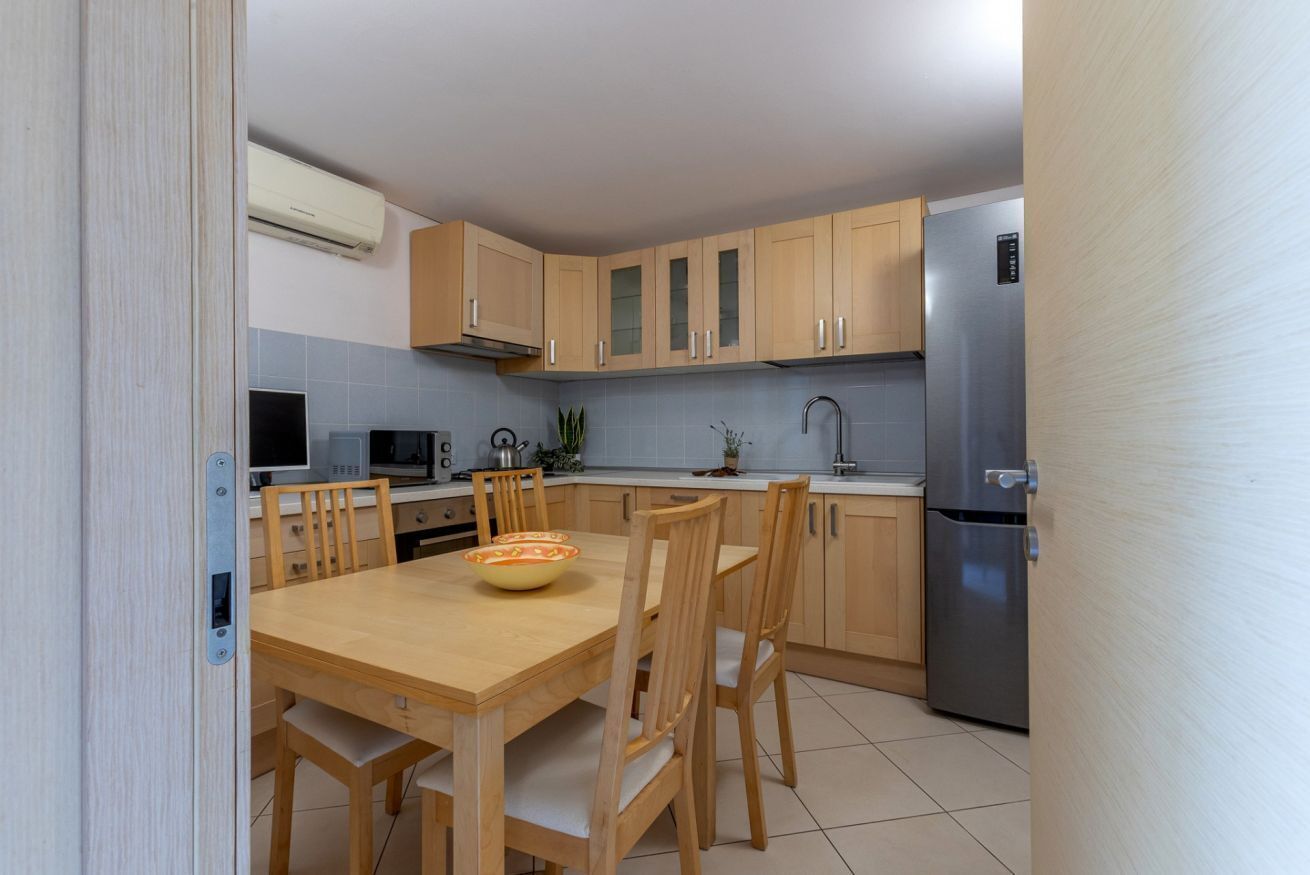 A modern kitchen with wooden cabinets, a stainless steel refrigerator, and a dining table with chairs.