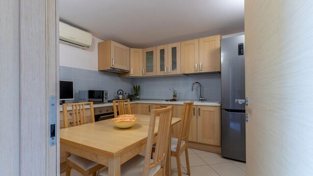A modern kitchen with wooden cabinets, a stainless steel refrigerator, and a dining table with chairs.