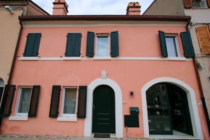 Un edificio de dos pisos con fachada color melocotón, contraventanas verdes y una puerta central arqueada.