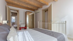 Un dormitorio con una cama, una mesita pequeña y una silla. El techo es de madera y hay un radiador blanco.