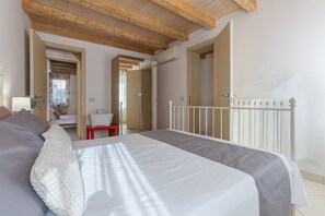 Un dormitorio con una cama, una mesita pequeña y una silla. El techo es de madera y hay un radiador blanco.