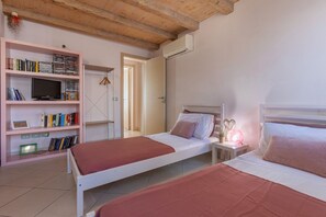 Un dormitorio con dos camas, una estantería, un televisor y un equipo de aire acondicionado.