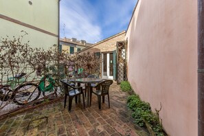 A brick patio with a table and chairs, a bicycle, and a building with a window. - GuestHost - A comfortable and welcoming 75 square meters apartment with a large courtyard and private entrance, perfect for six people, located on the ground floor of a renovated historic building facing the canal (NOT accessible by car).The property enj (Comacchio)