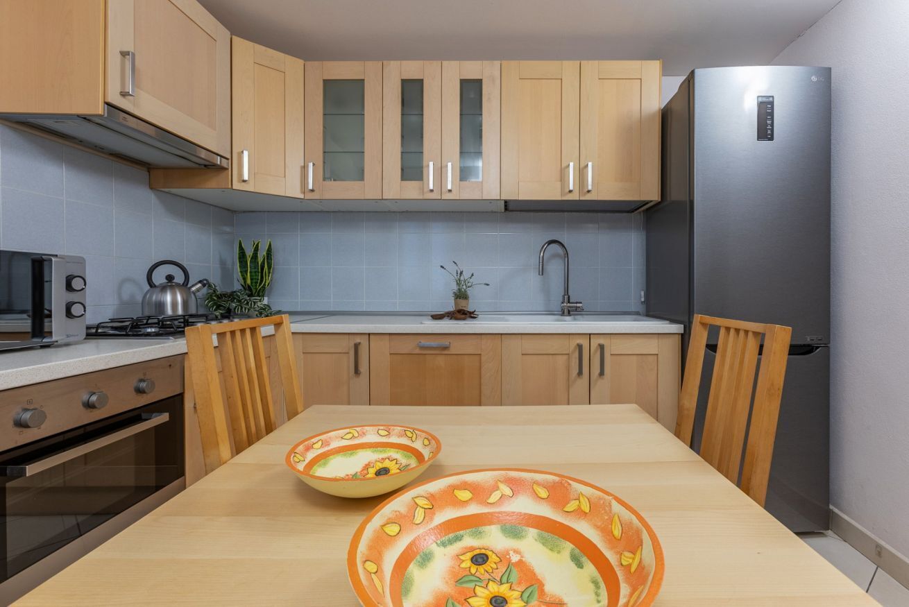 Una cocina moderna con armarios de madera, un refrigerador de acero inoxidable, una estufa a gas y una mesa de comedor con dos cuencos decorativos.