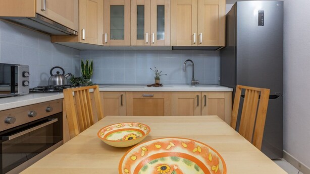 Una cocina moderna con armarios de madera, un refrigerador de acero inoxidable, una estufa a gas y una mesa de comedor con dos cuencos decorativos.