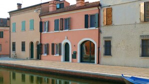 A canal-side building with arched doorways, a bicycle, and a blue boat.