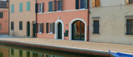 A canal-side building with arched doorways, a bicycle, and a blue boat.