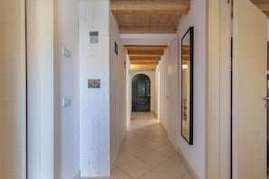 Un couloir avec des poutres en bois au plafond, un sol carrelé et une porte au fond.