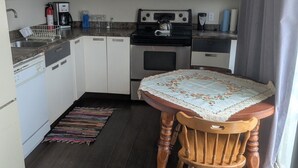 A compact kitchen with white cabinets, a microwave, a stove, and a dining table with a floral tablecloth.