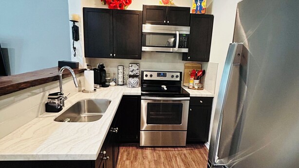 A compact kitchen with a central island, stainless steel appliances, and dark cabinetry. - Cozy, Piney Woods Barndo Studio in Silsbee--4 minutes from town. (Silsbee)