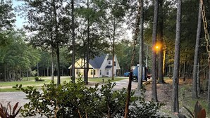 Una casa con porche, rodeada de árboles y un camino de grava.