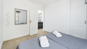 Habitación de hotel con dos camas, un espejo, una puerta y vista hacia otra habitación.