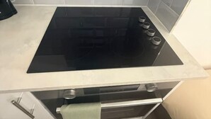 Een keuken met een zwart fornuis, witte kastjes en een betegelde achterwand.