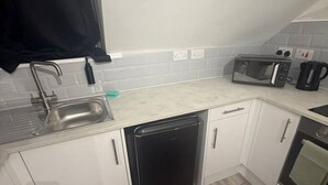 Een kleine keuken met witte kastjes, een vaatwasser, een magnetron en een koffiezetapparaat.
