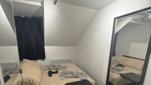 A small, modern bedroom with a single bed, a bedside table, a mirror, and a ceiling light fixture.