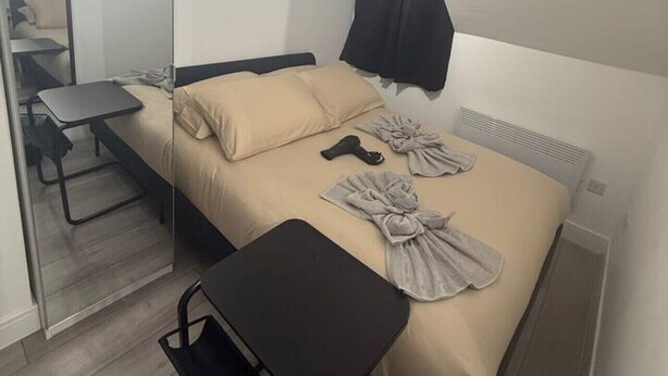 A modern hotel room with a bed, a small table, a chair, and a mirror.