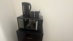 A black coffee maker with a kettle and two cups on top of a black refrigerator.