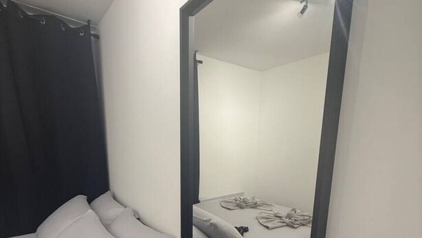 Ein kleiner, sauberer Raum mit einem Bett, einem Schreibtisch und einem großen Spiegel.