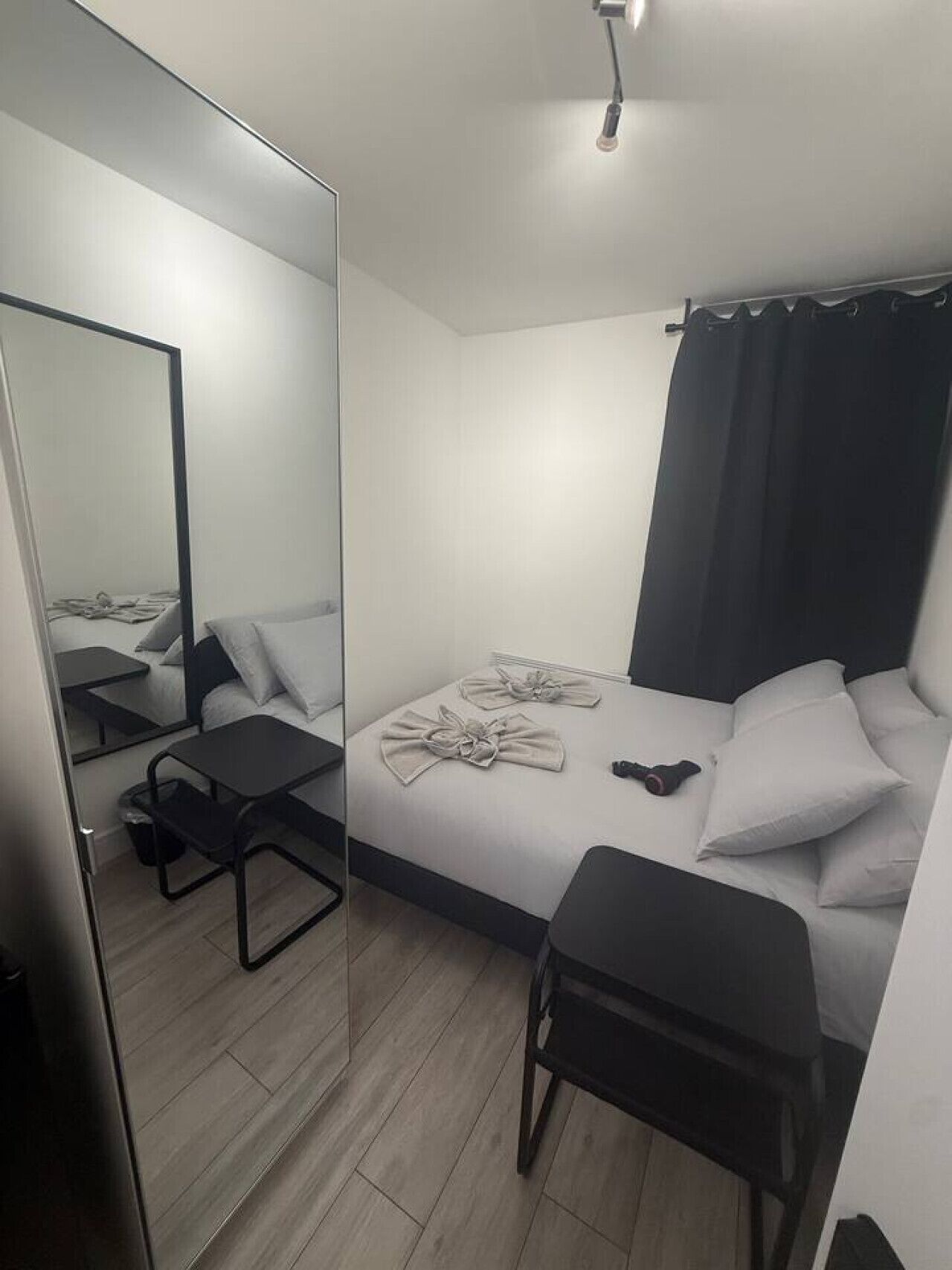 Et moderne hotelværelse med en stor seng, et natbord, en stol, et spejl og en loftslampe.