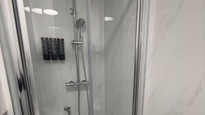 Eine Duschkabine mit Glaswänden, einer Handbrause und einem Wandarmaturen.