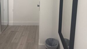 Ein Flur mit Glastür, Mülleimer und Spiegel an der Wand.