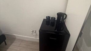 Ein kleines Zimmer mit einer schwarzen Kaffeemaschine und zwei Tassen auf einem kleinen Tisch, einer Steckdose an der Wand und einer Tür zu einem anderen Raum.