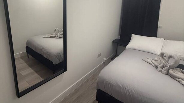 Ein Schlafzimmer mit einem großen Spiegel, einem Bett mit Handtüchern, einem Nachttisch und einem Mülleimer.