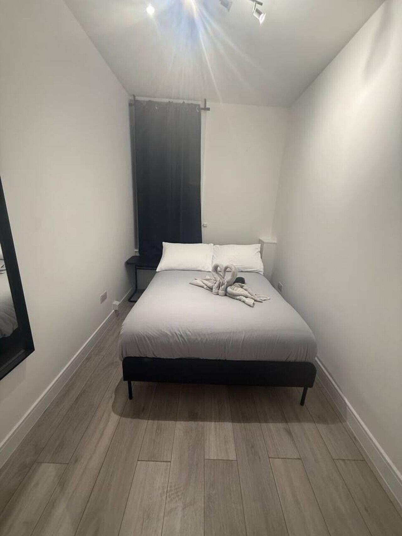 Une chambre à coucher avec un lit, une table de chevet, un miroir et une fenêtre avec un rideau.