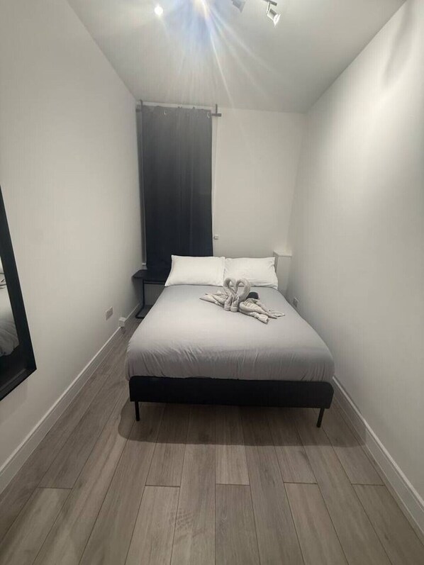 A bedroom with a bed, a nightstand, a mirror, and a window with a curtain. - Private room 5 min to Balham station (Greater London)