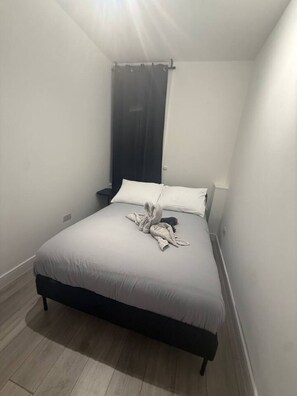 A small, neatly made bed in a room with a dark headboard and a window with a curtain. - Private room 5 min to Balham station (Greater London)