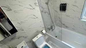A bathroom with a toilet, sink, and bathtub, all tiled with a marble-like pattern. - Central London room w kitchen (Greater London)